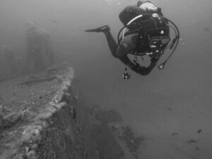 Advanced Season Pass 3 - a diver hovers alongside the deck of the Chester Poling wreck at a depth of 70 feet. Cunner fish appear in the lower right quadrant over the sand.